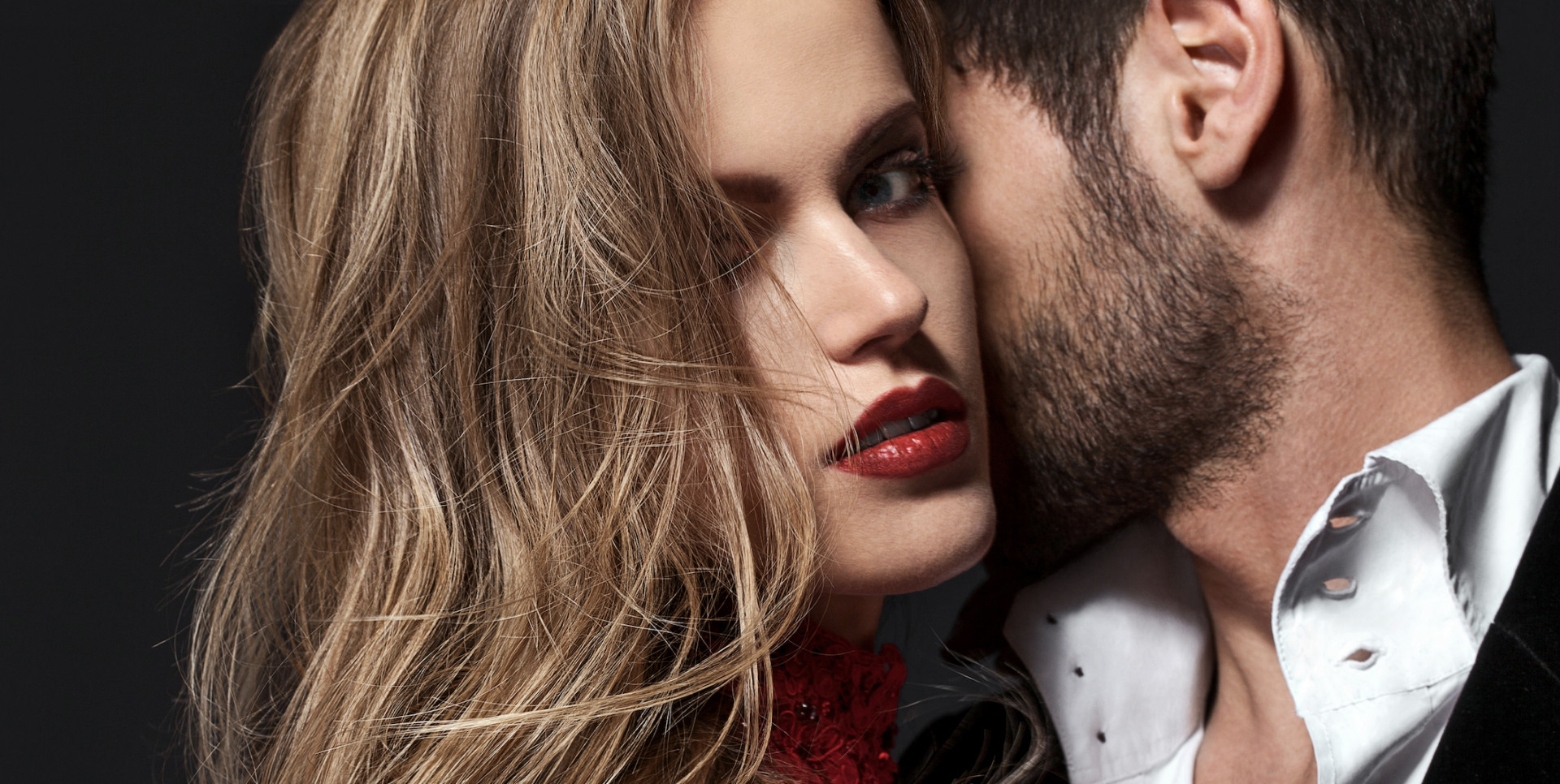 woman with red lipstick hugging man who whispers in her ear