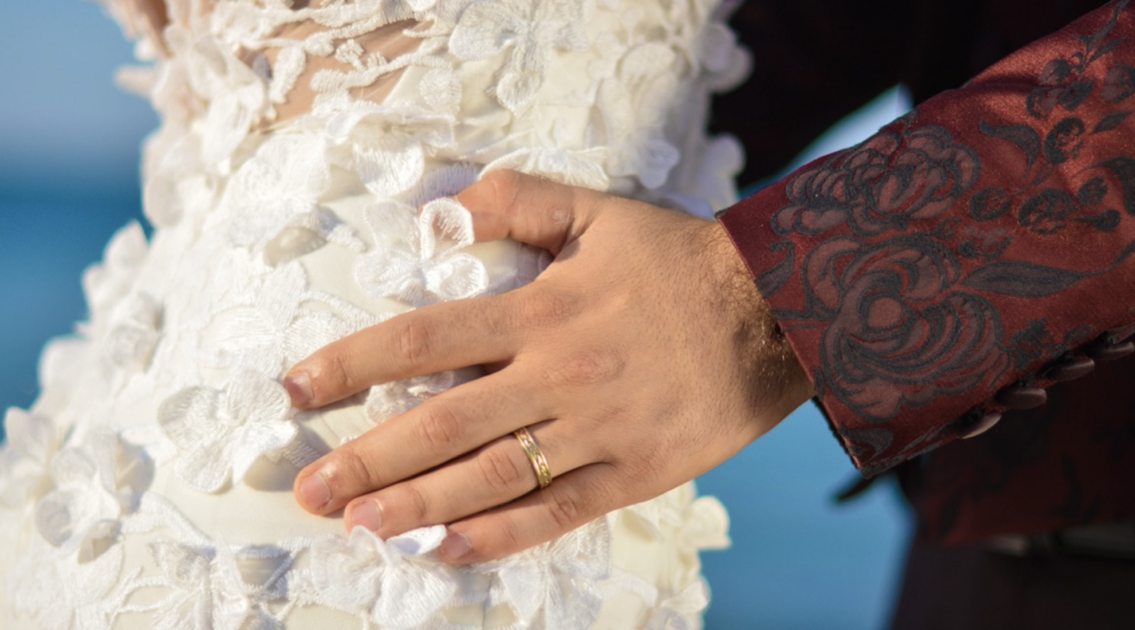 man's hand wearing ring on girl in wedding gown's hips.