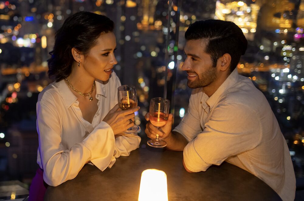 couple on date holding wine with nighttime view of city