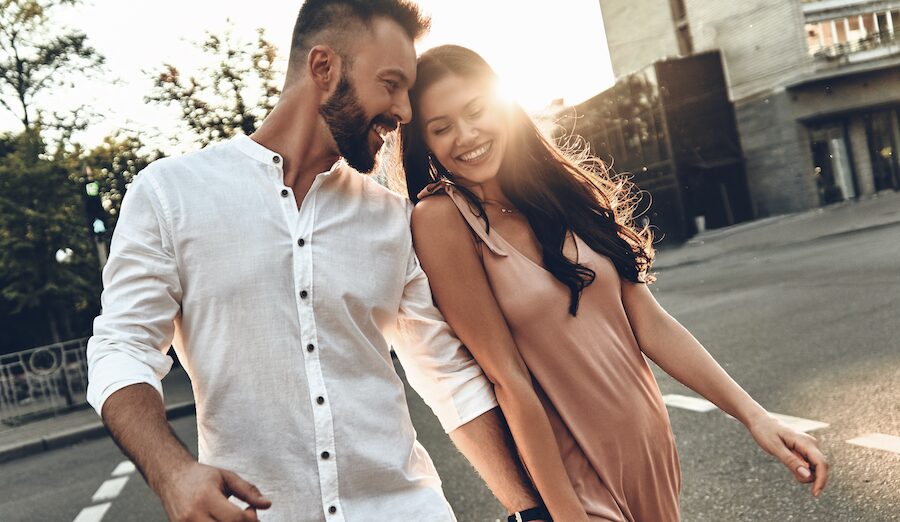 couple holding hands walking down street with sunset behind them