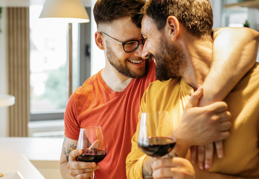 two men drinking wine and holding each other very closely.